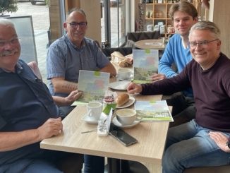 Vier Männer mit Broschüren im Café sitzend.