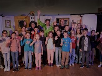 Gruppenfoto von Kindern und Erwachsenen auf Theaterbühne.